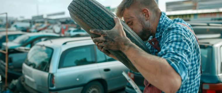 Repairman pumps the tire on car scrapyard